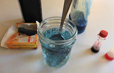 A picture of small bottles of food coloring and water in a glass jar.
