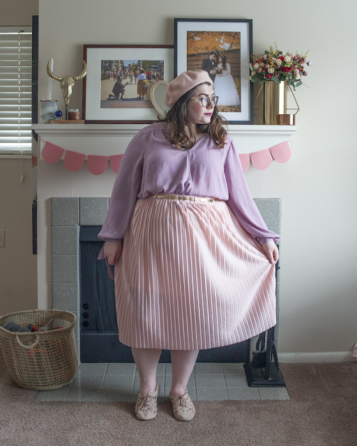 An outfit consisting of pastel pink beret, pastel lavender wrap blouse tucked into a pastel pink pleated midi skirt and pastel pink skirt.