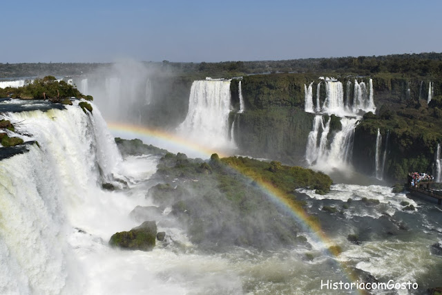 foto das cataratas do Iguaçu com queda d'água do lado esquerdo e do lado direito com arco-íris no meio  