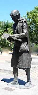 Escultura de la chica leyendo a la entrada del metro de Aluche. A sus pies una placa recuerda a Yolanda González