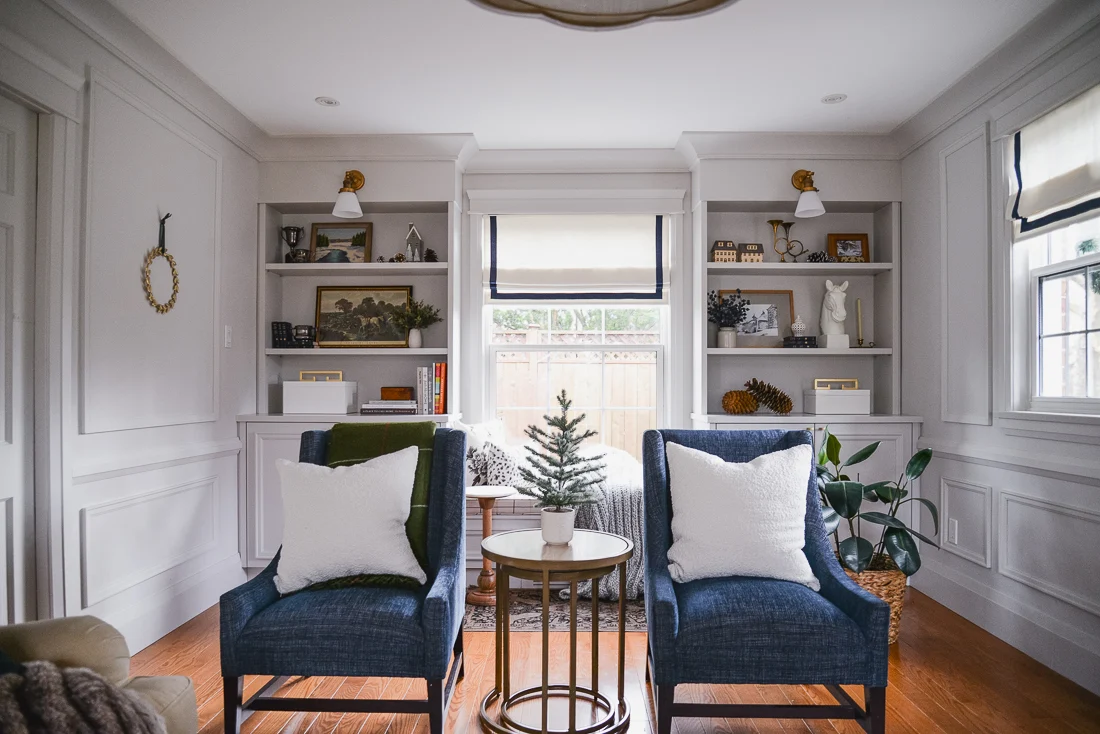 winter living room with window seat, built in bookcases and pair of blue armchairs