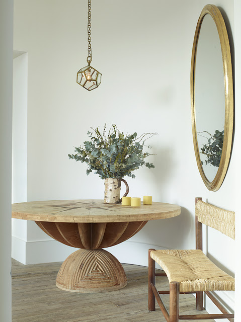 carved wood table in entry with oversized gold round mirror