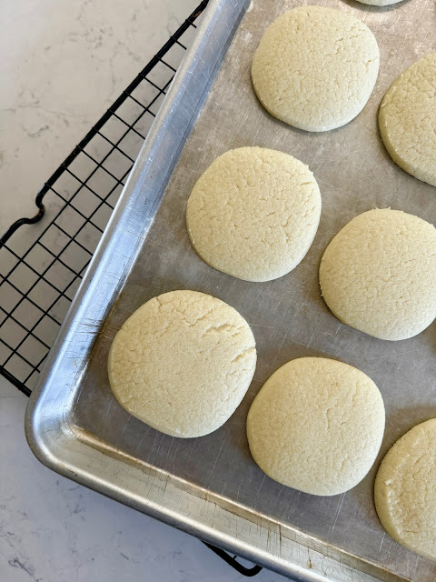 Sugar cookies on a metal sheet pan on a wire baking rack.