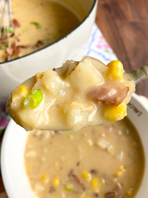 Up close shot of spoon holding potato chowder with pot and white bowl in the background.