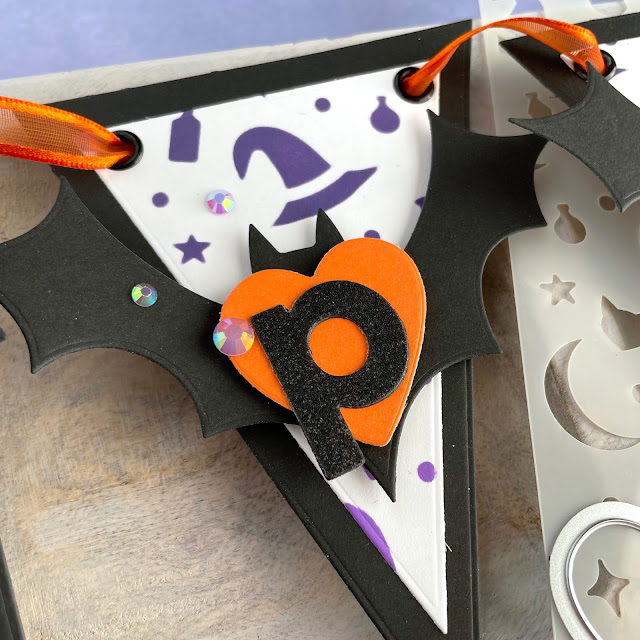 Spooky Halloween Banner created with: Scrapbook.com halloween bats die, magic potion stencil, glitter paper metals, smooth cardstock rainbow, domed foam blending tool, nested hearts, bold basic alpha, nested triangle banner; Tim Holtz distress oxide villainous potion, wilted violet; Pinkfresh jewels