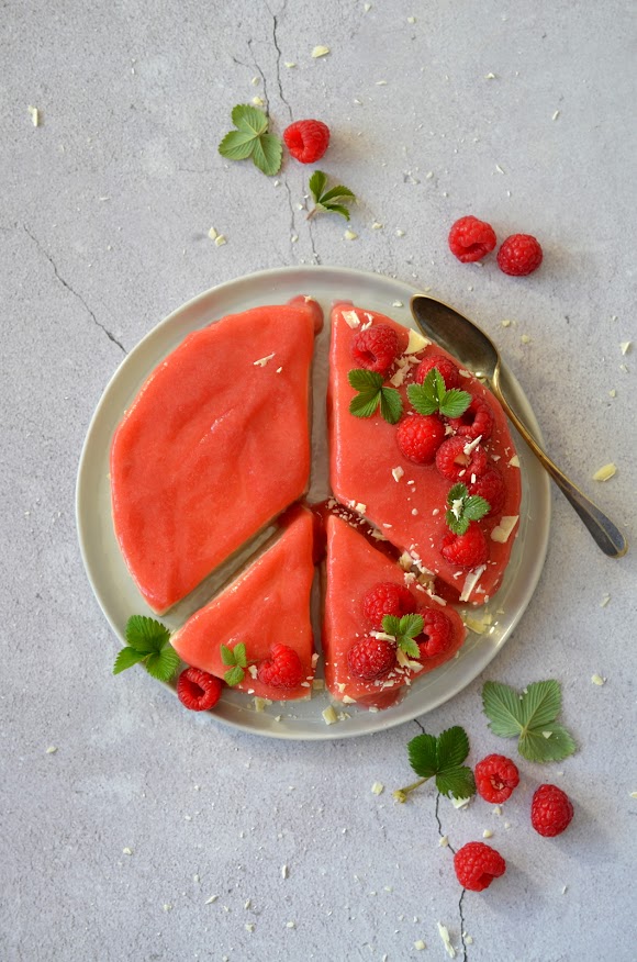 Ein runder Pudding ist so zerteilt, dass er wie ein Peace-Zeichen aussieht. Der Pudding ist mit roter Fruchtsauce, Himbeeren und weißer Schokolade dekoriert.