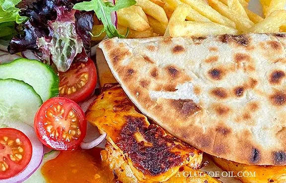 Greek flatbread with grilled halloumi and baby salad leaves with tomato and cucumber.