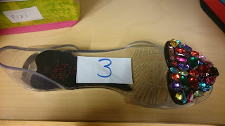 En genomskinlig plastsko med glitterstenar som står i en hylla. På skon står siffran 3.