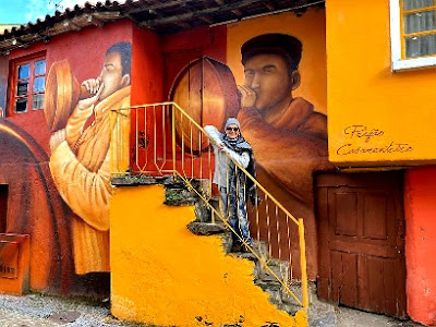 mulher numa escada de uma casa de Podence toda pintada com dois personagens do Carnaval de Podence