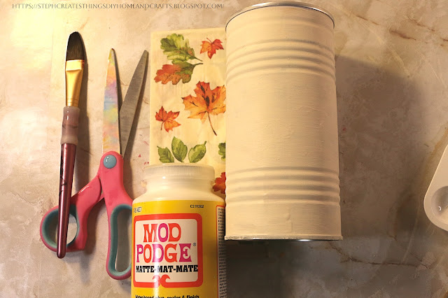 Paintbrush, scissors, decorative napkin, Mod Podge, and metal can on a table
