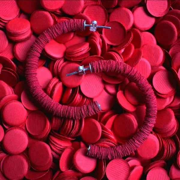 pair of red paper disc earrings atop a vast number of punched red paper discs.