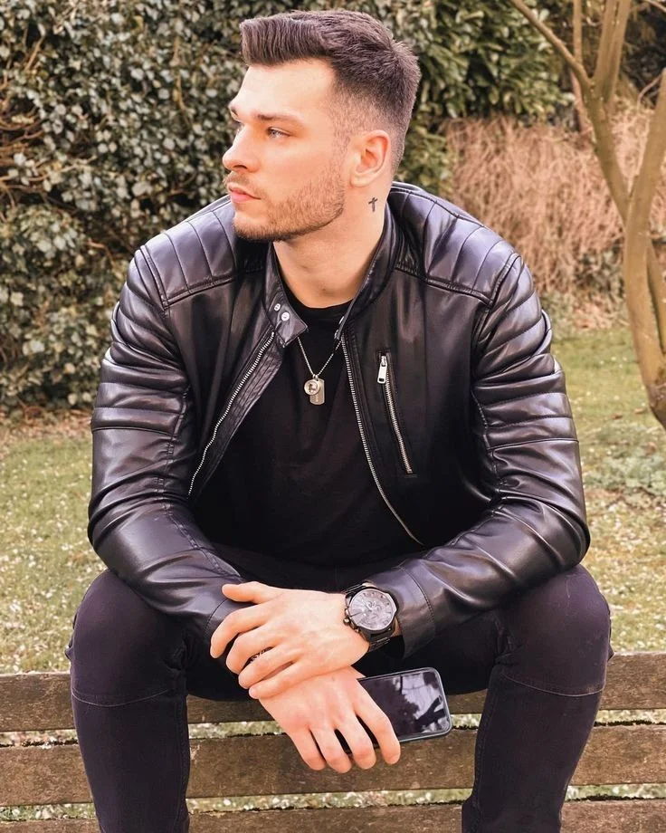 Sexy man sitting on a bench outside wearing black leather biker jacket and jeans