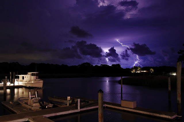 A purple storm cloud covered sky at night over a harbor with a bolt of lightning.