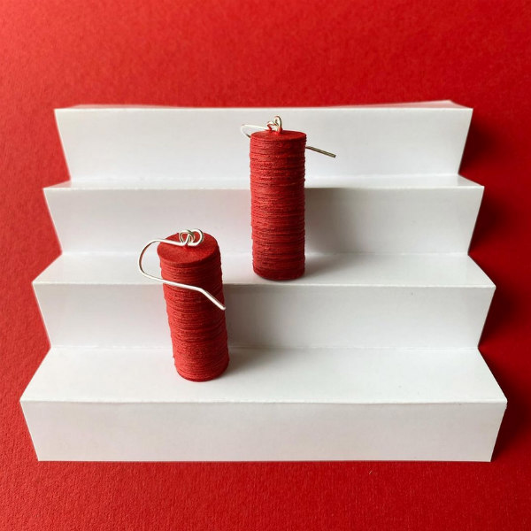 pair of columnar red earrings made of punched paper circles with silver ear wires positioned on folded white paper steps