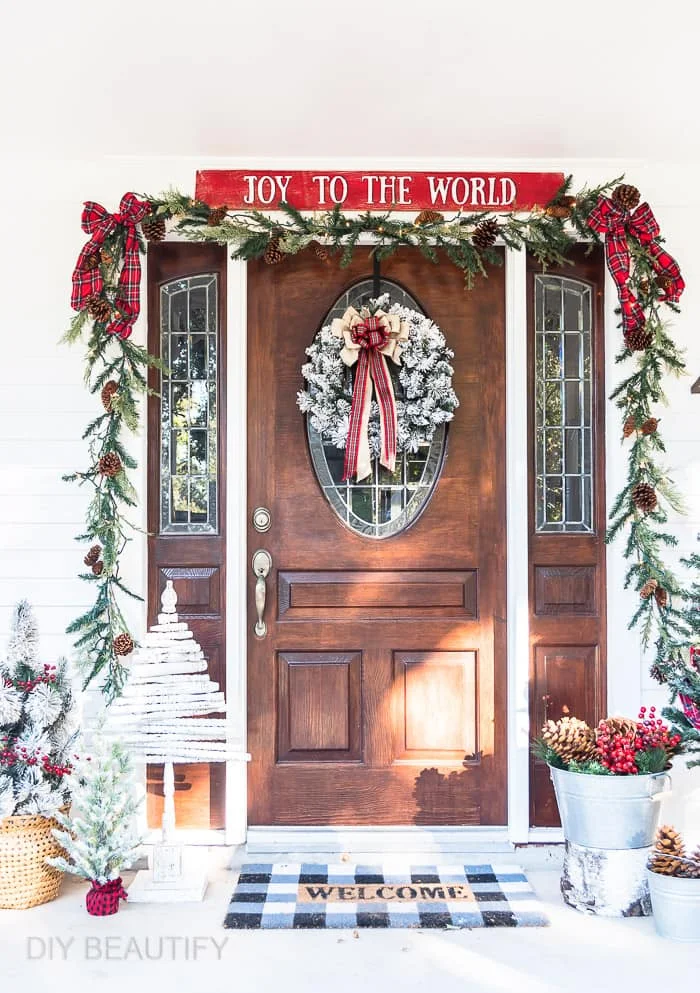 front porch with fence board Christmas sign, plaid boxes, spindle tree, garland