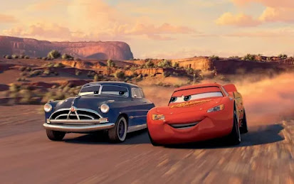 Doc Hudson, a blue 1951 Hudson Hornet, and Lightning McQueen, a red racecar, driving in a deserty area.