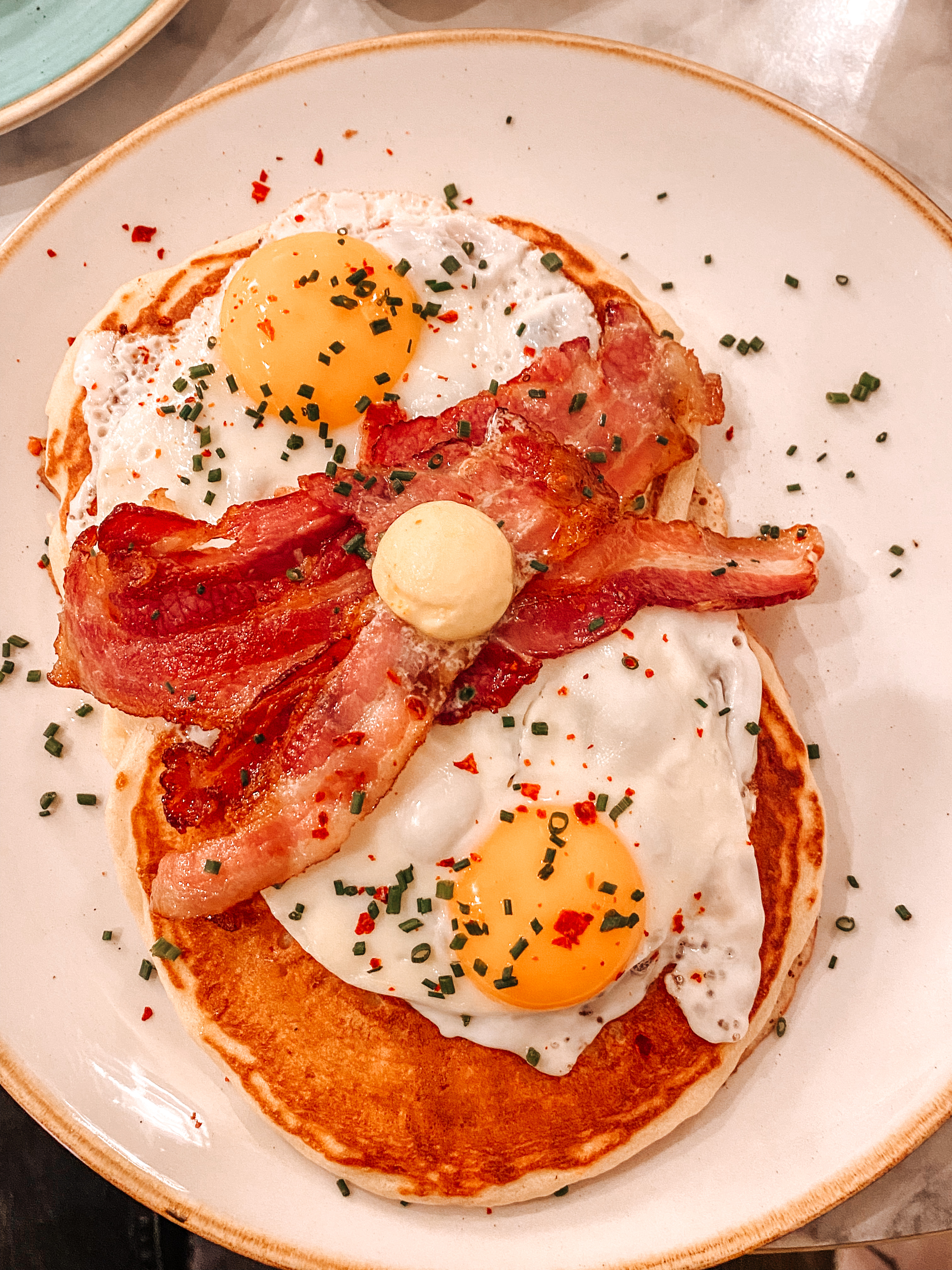 assiette blanche avec des pancakes et dessus du bacon et des oeuf au plat dans le restaurant immersion Paris