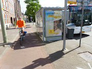 The bus shelter is very close to the edge of the Further down past the bus . (bus stop and cycletrack )