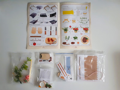 One-twelfth scale modern miniature kit pieces for a vase and flowers, chopping board, knife and apples, steak dinner, toaster and grocery bag.