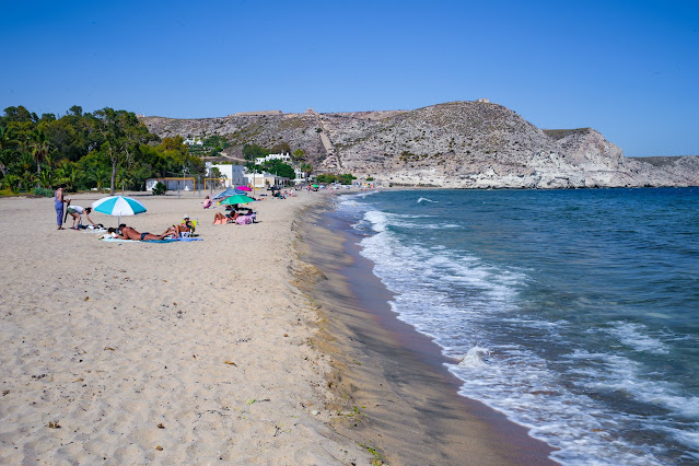 Playa de arena fina con turistas y las montañas al fondo