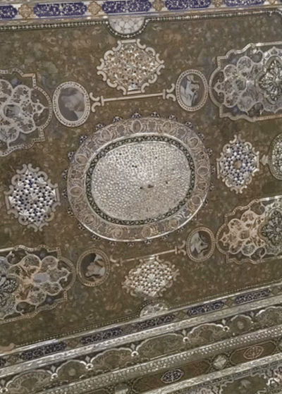 A slow panning shot reveals an ornate Persian ceiling filled with mirror mosaics, miniature portraits, and floral designs, shimmering under ambient light.