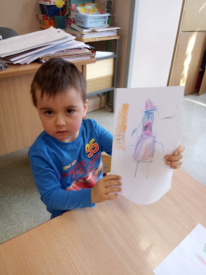 Na zdjęciu chłopiec pokazuje swoją pracę plastyczną