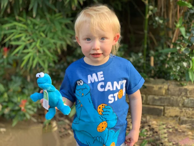 A toddler in a Cookie Monster t-shirt with Cookie Monster small plush