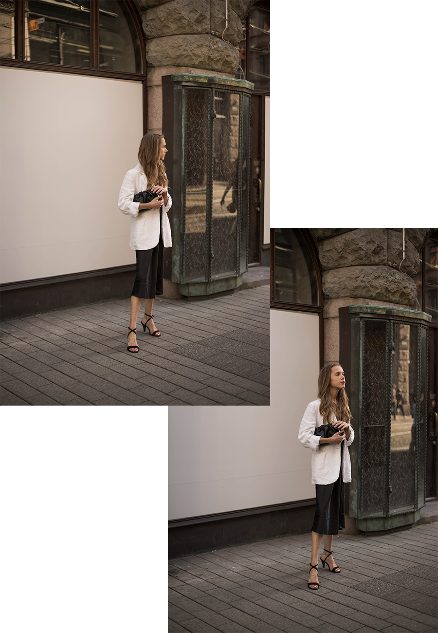 Nainen seisomassa kadulla yllään musta satiinimekko ja valkoinen bleiseri