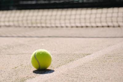 Grön tennisboll på grusbana med nät i suddig bakgrund.