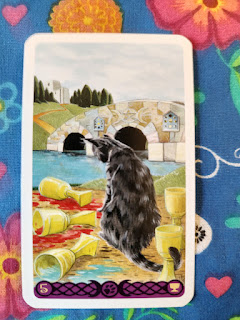 Five of Cups card. A dark colored cat looks sad at three spilled cups. Two cups still stand