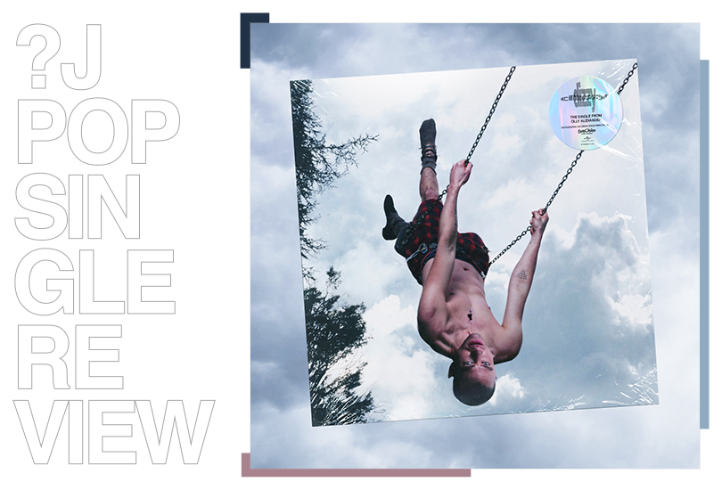 Vinyl of Olly Alexander’s “Dizzy”, superimposed over a backdrop of grey clouds.  The cover art for “Dizzy” features a shot of Olly Alexander topless and swinging on a playground swing. The shot has him upside down, with trees visible on the left and the sky looking grey, as though a storm is brewing.