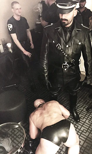 Master in leather uniform stands gloating as slave licks feet