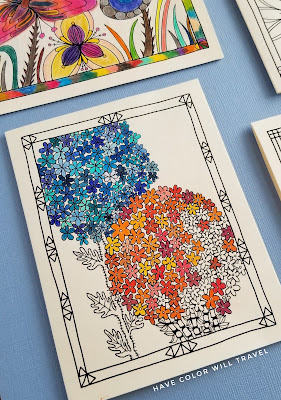 A colorable flower illustration card is partially colored in both cool and warm colors. It lies on a textured blue background.