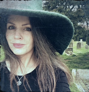 Grey filtered image of a woman wearing a green witch's hat and a pentagram necklace in a black top