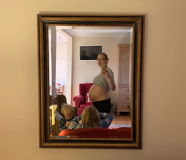 A mobile photo take on 38 week pregnant bump in a mirror with children in the foreground