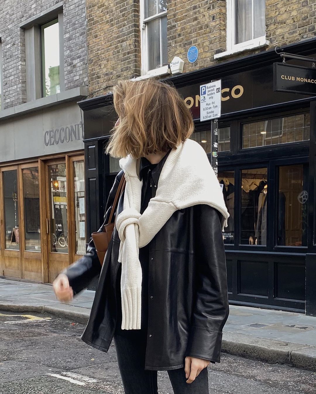 How a British Fashion Girl Wears a Leather Shirt Jacket — Lizzy Hadfield Winter Outfit With Black Shacket and White Sweater Tied Over the Shoulders