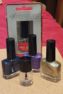 Three regular size bottles of Expressions nail polish in dark blue, purple and gold, with a smaller bottle of top coat in front and a box with a larger bottle of top coat behind.