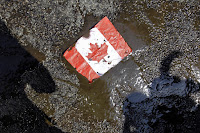 A placard with the Canadian flag rests on the ground covered in oil as demonstrators conduct a die-in to protest against the Keystone Pipeline and the Alberta Tar Sands. (Photo Credit:  AP / Nam Y. Huh) Click to Enlarge.