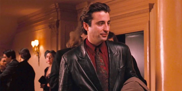 From waist upward sexy Andy Garcia wearing black leather blazer with red shirt and gold tie underneath