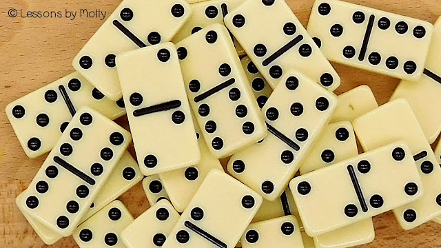 Dominoes spread out on a surface. The dominoes display different combinations of dots on their halves, and they are arranged in a random and disorganized manner.