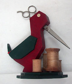 red wooden bird holding scissors, with spools of thread on the base