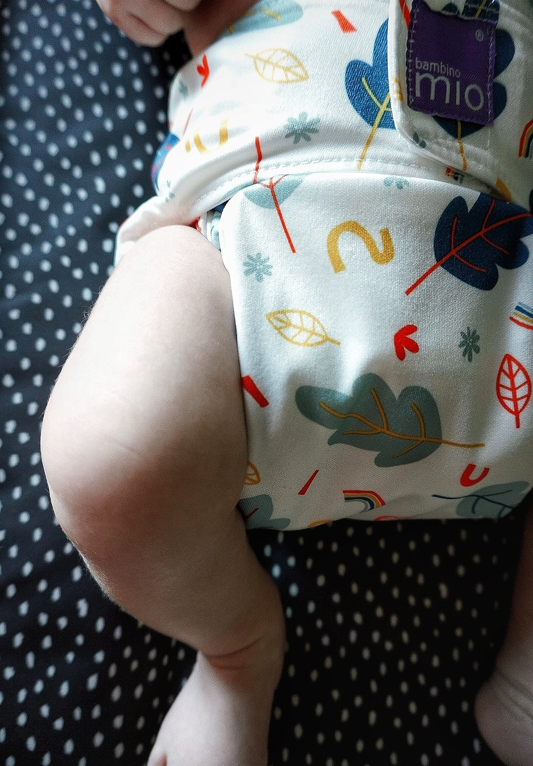 A baby's leg on a changing mat sticking out of a reusable nappy with a leaf design on it