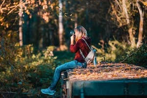 A lady that sit down holding camera in his hand shooting inside the forest