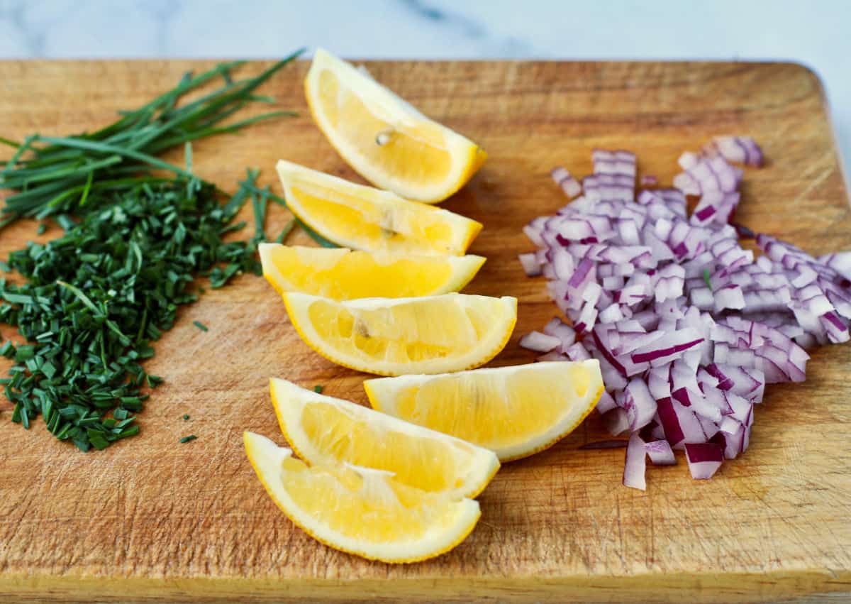 Chives, lemons, and onions on a wood board.