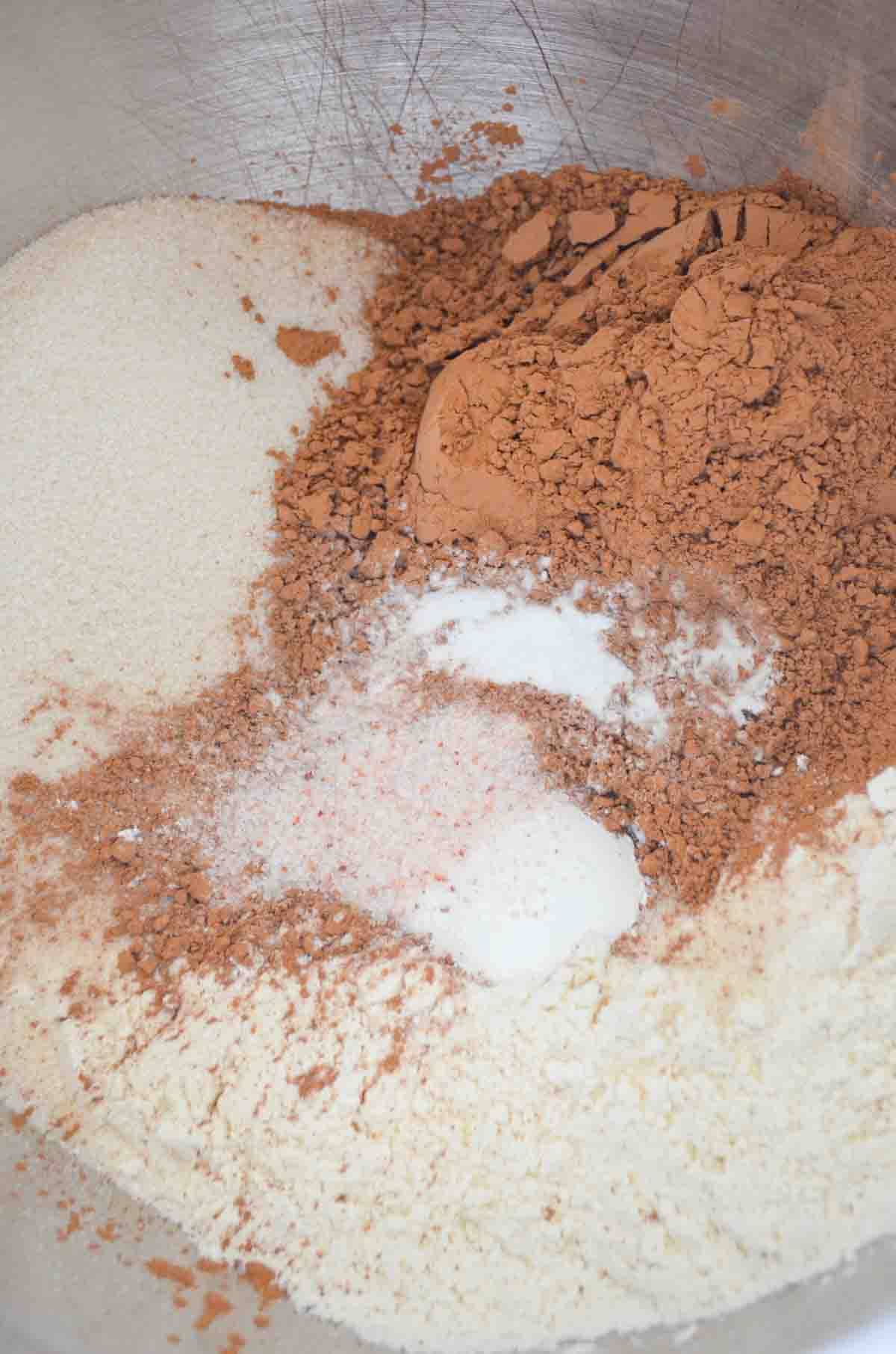 A down shot of flour, sugar, cocoa powder, baking soda, baking powder, and salt in a stainless steel mixing bowl.