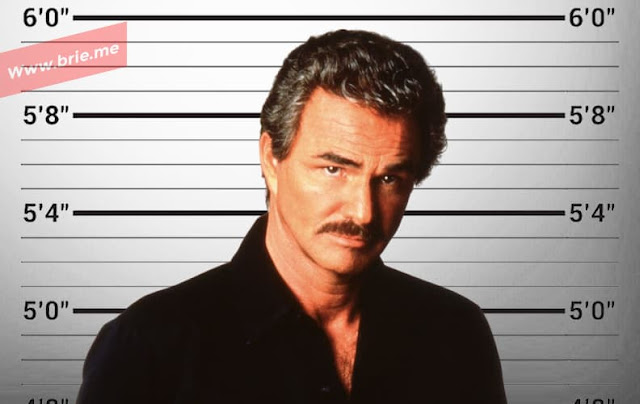 Burt Reynolds posing in front of a height chart