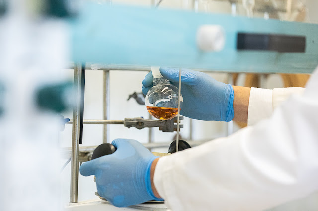 Close up of a person in a white lab coat and blue rubber gloves performing a chemistry experiment in a science lab.