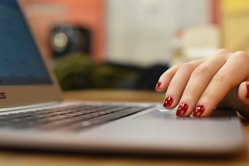 Una mano con las uñas pintadas sobre una laptop.