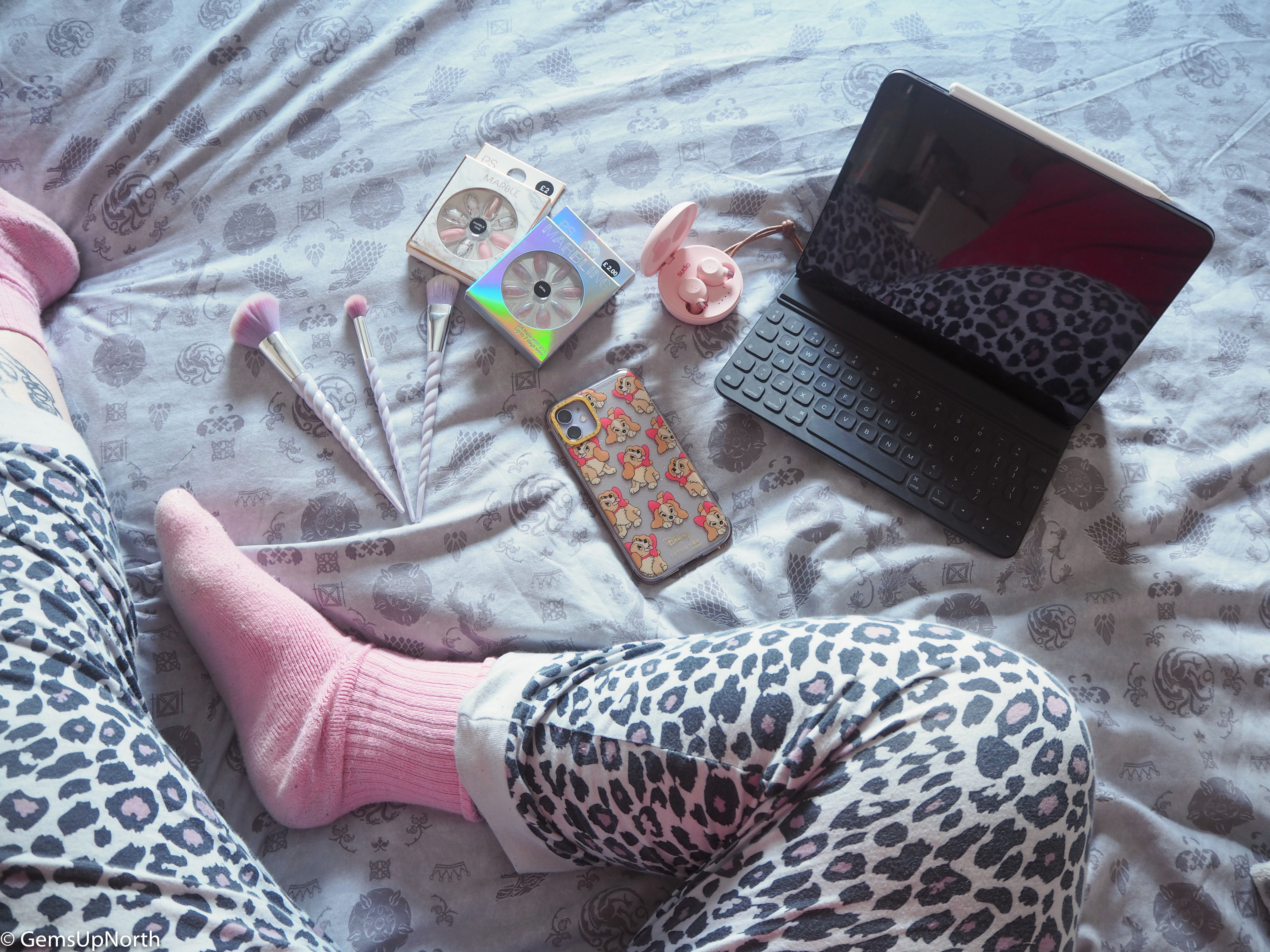 Shot of GemsUpNorth's leg with leopard print PJs on, FEM Sudio ear buds, iPad, Phone and some beauty bits on a GOT bed set
