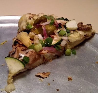 Single piece of Round Table's 'Gourmet Veggie' pizza, featuring artichoke hearts, zucchini, spinach, mushrooms, garlic, red and green onions on Creamy Garlic Sauce. There are no tomatoes on this slice of pizza.